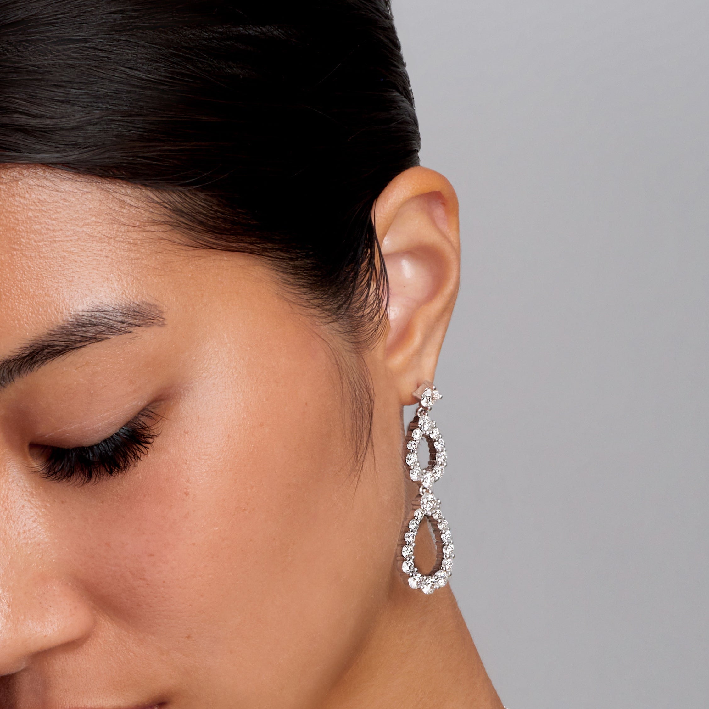 Woman wearing silver jewelry including earrings, necklace, and rings on a gray background
